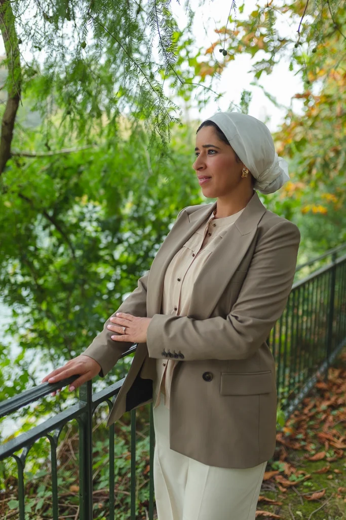 Asma Dana debout à l'extérieur, la main appuyée sur une rambarde, regardant au loin.