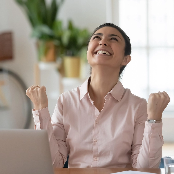 Jeune femme serrant les poings et regardant vers le haut, souriante, dans une posture de victoire.
